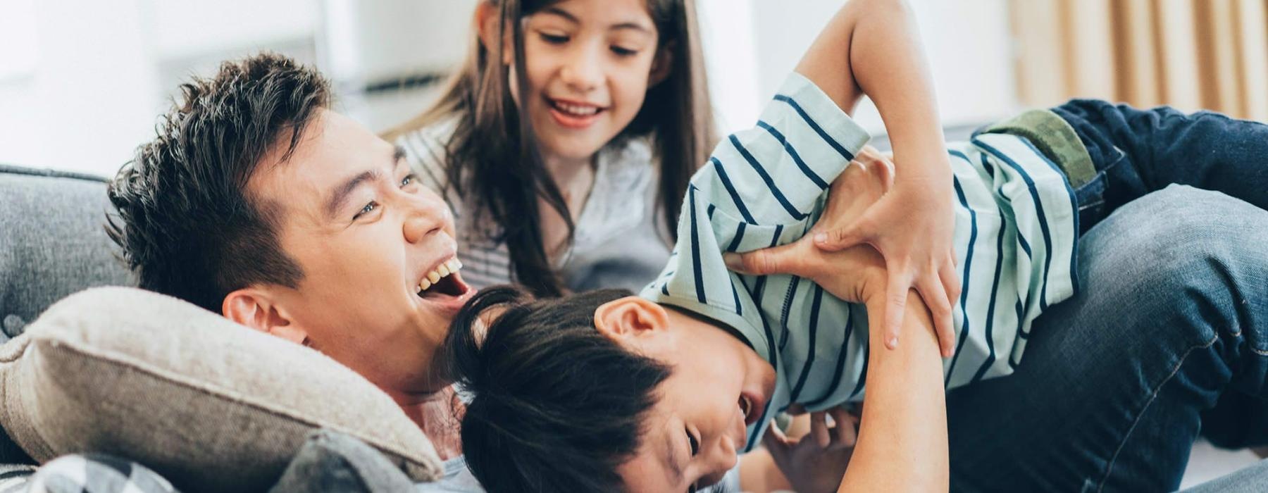 father plays on a couch with his young children